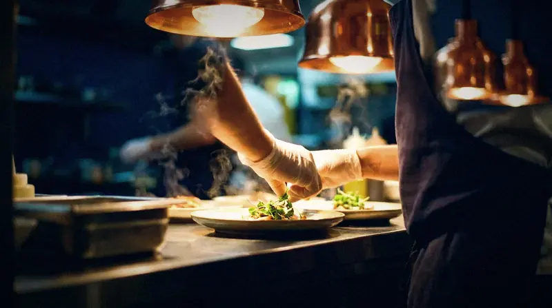 A chef plating at the pass under copper lamps during service